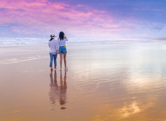 Two women walking on the beach at sunset.