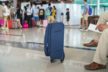 Travel suitcase in airport departure lounge with queue of passengers on background