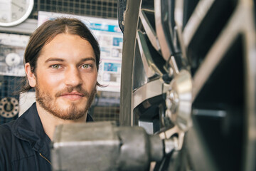 Fototapeta na wymiar Handsome mechanics in uniform are working in auto service with alloy wheel. Car repair and maintenance in store.