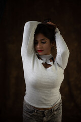 Studio portrait of a beautiful and young Indian Bengali female model in white cold shoulder top and jeans hot pant. Indian fashion and models