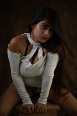 Fototapeta premium Studio portrait of a beautiful and young Indian Bengali female model in white cold shoulder top and jeans hot pant. Indian fashion and models