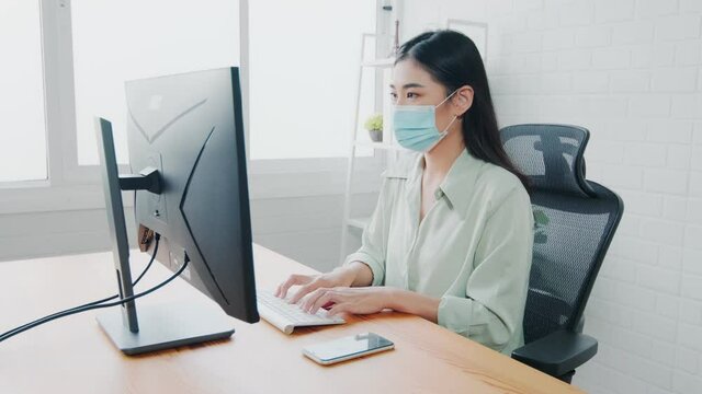 Beautiful Asian business woman work at home modern office, wearing medical face mask coughing, protection from COVID-19 pandemic smart plan strategies using computer internet networking technology