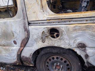Closeup of passenger side of abandoned and burned car showing gas tank, melted tire and rear quarter panel