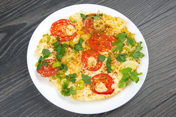 cooked fried omelet with herbs and vegetables in a white plate on a wooden table