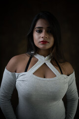 Studio portrait of a beautiful and young Indian Bengali female model in white cold shoulder top and jeans hot pant. Indian fashion and models