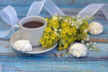 Obraz na płótnie Canvas bouquet of yellow and white spring flowers, a cup of coffee, meringues, nylon ribbon on a blue wooden background