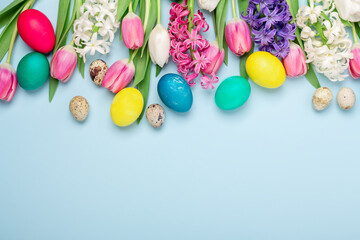 Fototapeta na wymiar Multicolored eggs and spring flowers tulips and hyacinths on a blue background. Easter concept. Copy space