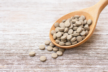 Green natural herbal medicine tablet in wooden spoon isolated on wood table background. 