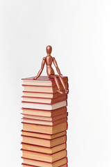 A wooden man sits on a stack of books. Scientific research. The concept is to search for information in books.