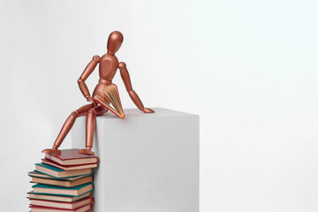 A wooden man sits on a stack of books. Scientific research. The concept is to search for information in books.