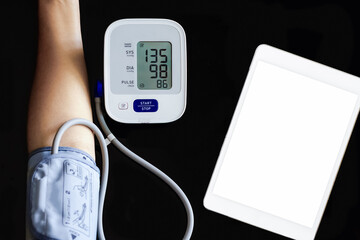 Woman takeing blood pressure by using digital sphygmomanometer with digital tablet computer on the desk. Medical and healthcare concept. Hypertension concept. Top view.