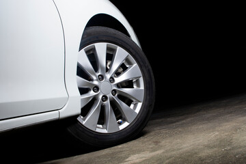 Alloy wheels of a white car are turning on the cement road of parking lot with copy space