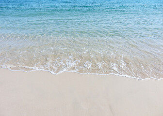 Fototapeta na wymiar Foamy waves on a sandy beach with blue sea water at a tropical beach