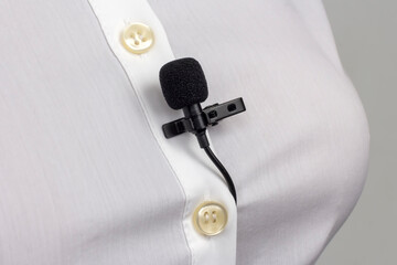 The lavalier microphone is secured with a clip on a women's shirt close-up. Audio recording of the...