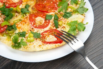 cooked fried omelet with herbs and vegetables in a white plate on a wooden table
