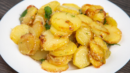 cooked fried potatoes with herbs and vegetables in a white plate on a wooden table
