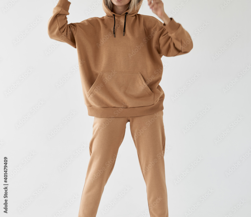 Poster girl wears light brown hoodie and pants. isolated photo of women wearing nude color fleece textile outfit.