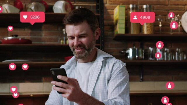 Happy positive adult businessman standing in kis modern kitchen using application on mobile phone. Smartphone user interface. Like and comment icons. Animation.