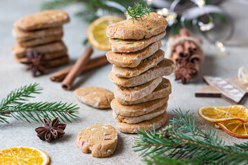 Stacked spicy butter cookies with candied fruits, cinnamon sticks and anise. Festive Christmas or New Year background with fir branches and dried oranges slices.
