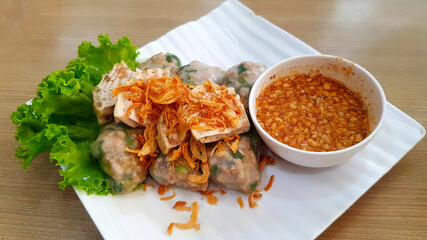 Vietnamese steamed rice-skin dumplings, green cabbage leaf and fried onion on top with sweet peanut bean sauce in white dish or plate. Asian food on wooden table and Famous meal in Vietnam.