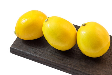 Three fresh juicy yellow lemons lie on a black wooden cutting board. Isolate on a white background.