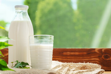 Bottle and glass of milk on wooden table against blurred foliage background