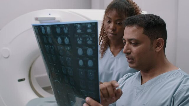 Medium shot of male radiologist in scrubs holding CT scan of brain and talking to female colleague