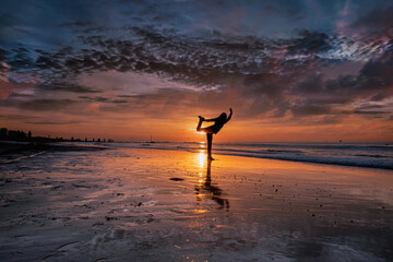 Silhouette of a young woman practicing yoga on the beach during a beautiful golden, purple sunset