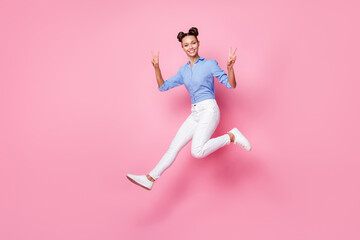 Fototapeta na wymiar Full length body size photo carefree childish girl jumping showing v-sign gesture in casual outfit isolated on pastel pink color background