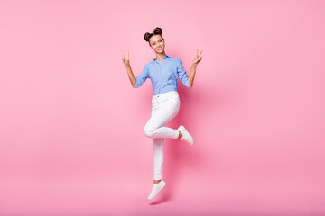 Full length body size photo of funny girl jumping smiling showing v-sign gesture isolated on pastel pink color background