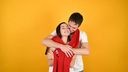 Lovely young couple hugging. Portrait of happy young couple with red warm scarf in front of yellow background. Valentine's Day celebration