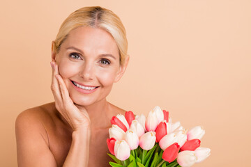 Cheerful middle aged woman enjoy her anti wrinkle tightening hold 8 march bunch isolated beige pastel color background