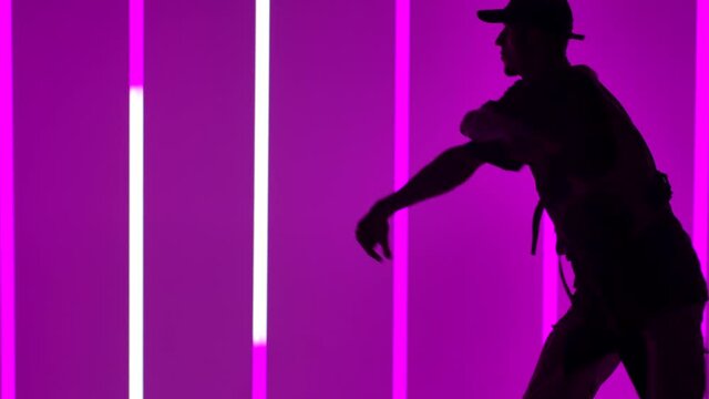 Young hip hop dancer performing dance show in studio with bright neon lights. Street dancing as a way of life. Silhouette. Close up. Slow motion.