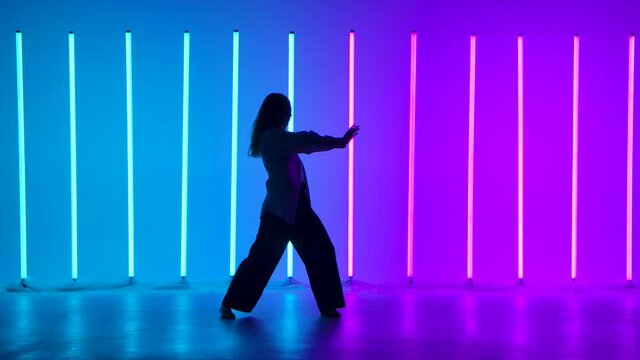 Young woman dancer dancing contemporary in the studio against the background of multicolored neon tubes. A talented girl performs a dance with elements of modernity. Silhouette. Slow motion.