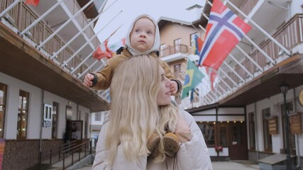 woman with her son on her shoulders stands in the street with flags