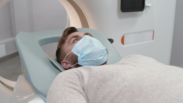 Slowmo shot of male patient in face mask lying still on treatment couch moving out of CT scan