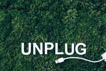 Word Unplug, white internet usb adapter on moss, green grass background. Top view. Copy space....