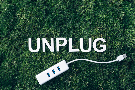 Word Unplug, white internet usb adapter on moss, green grass background. Top view. Copy space. Banner. Biophilia concept. Nature backdrop