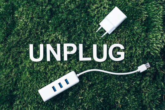 Word Unplug, white internet usb adapter on moss, green grass background. Top view. Copy space. Banner. Biophilia concept. Nature backdrop