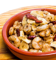 Prawns with garlic and cayenne in a ceramic bowl on a wooden tray