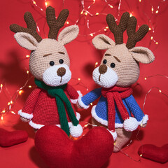 Valentines day, love and relationships. Two cute knitted amigurumi deer on red background with garland and red handmade hearts. Charming minimalistic Christmas and new year holiday background.