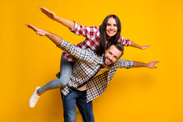 Portrait of nice lovely cheery couple piggy backing having fun like plane isolated over bright yellow color background