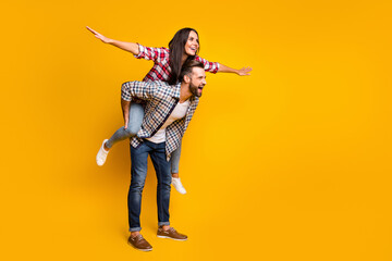 Full length body size view of lovely cheerful couple piggy backing having fun fooling copy space isolated over bright yellow color background