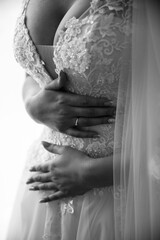 Beautiful bride on a gray background. On the woman is a long wedding dress with lace and an open back. Bouquet in hands.