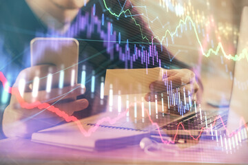 Double exposure of man's hands holding and using a phone and financial graph drawing. Analysis concept.