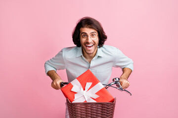 Portrait of young happy excited handsome guy man male ride bike with red box gift isolated on pink color background