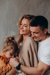 Photoshoot of a happy young family. Dad, mom and daughter. Studio photography.