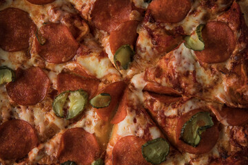 Delicious pizza with salami and cucumbers on a dark stone table.