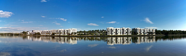 Beautiful panoramic view of a river with reflections of modern apartment buildings, blue sky and trees on water, Parramatta river, Wilson Park, Silverwater, Sydney, New South Wales, Australia

