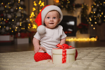 Fototapeta na wymiar Cute baby in Santa hat with Christmas gift on floor at home